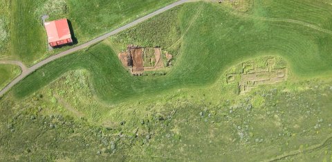 Loftmynd tekin með þyrlu, austan við túnið, sem sýnir afstöðu kirkjugarðsins gagnvart núverandi bæjarhúsum á Hofstöðum og rúst víkingaaldarskálans í ágúst árið 2013. ©Fornleifastofnun Íslands ses.